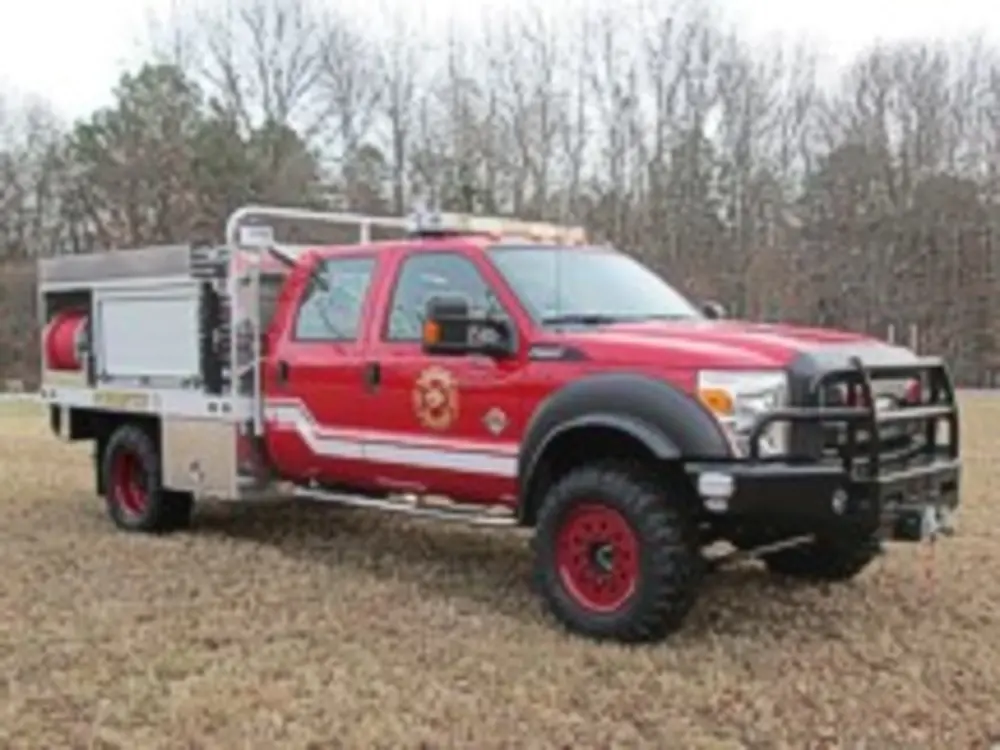 Exterior view of small fire truck showing cab, body compartments, and wheel/tire area.