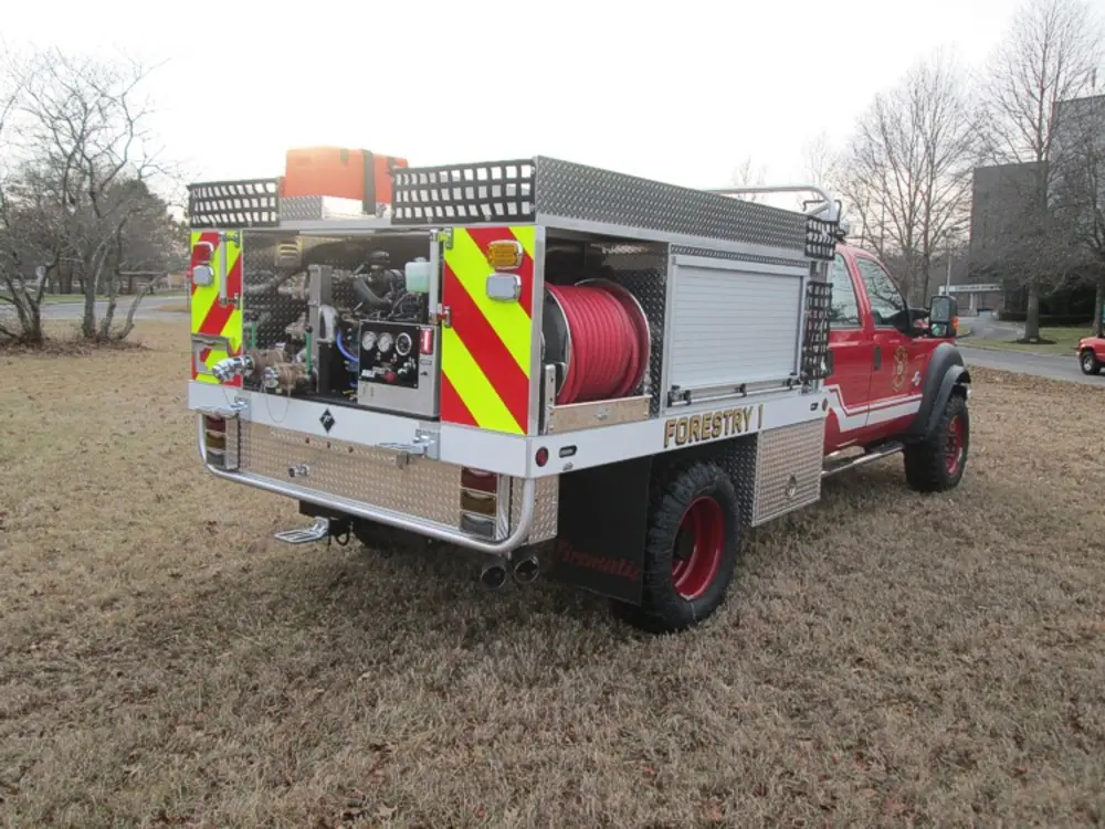 Exterior view of small fire truck showing cab, body compartments, and wheel/tire area.