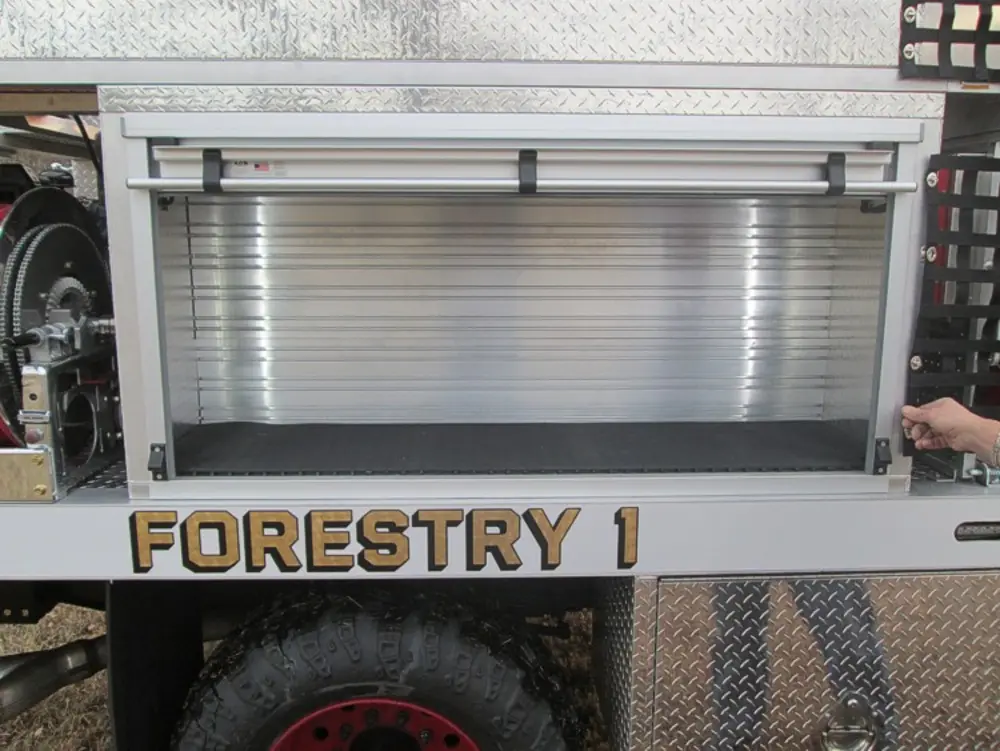 Exterior view of small fire truck showing cab, body compartments, and wheel/tire area.