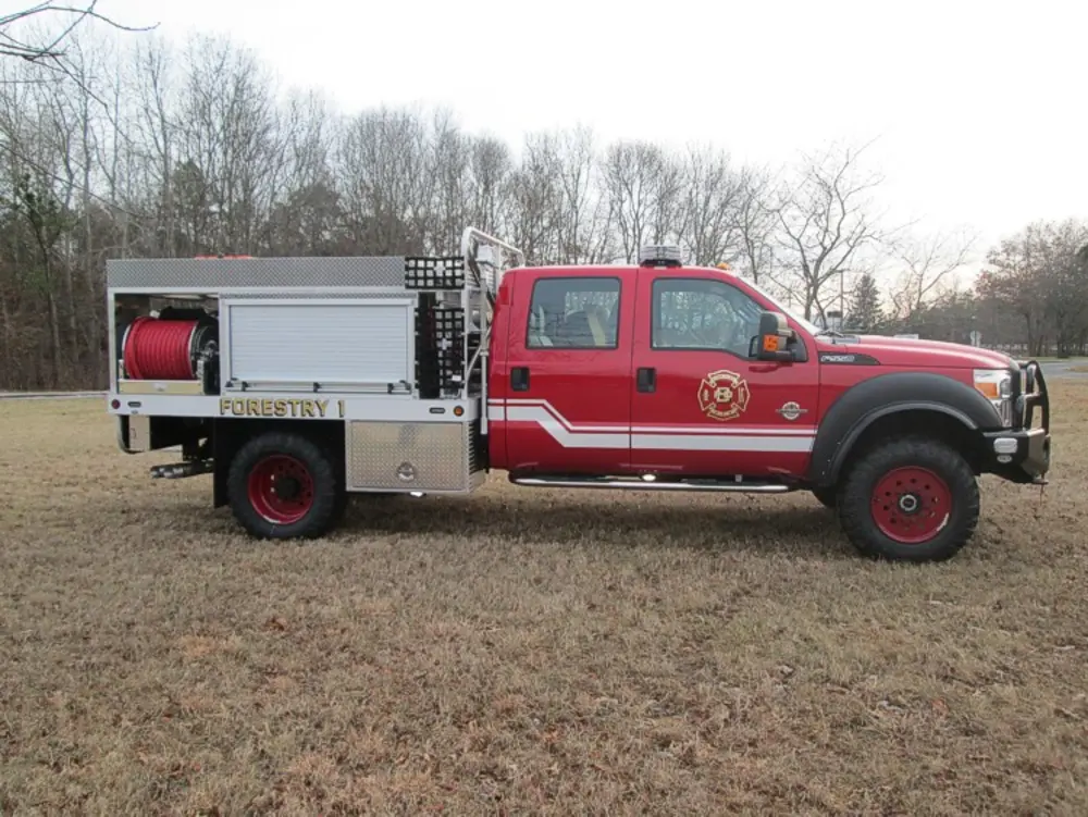 Exterior view of small fire truck showing cab, body compartments, and wheel/tire area.