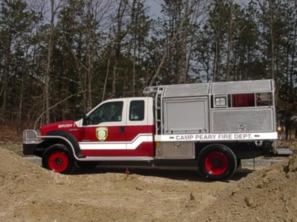 Exterior view of small fire truck showing cab, body compartments, and wheel/tire area.
