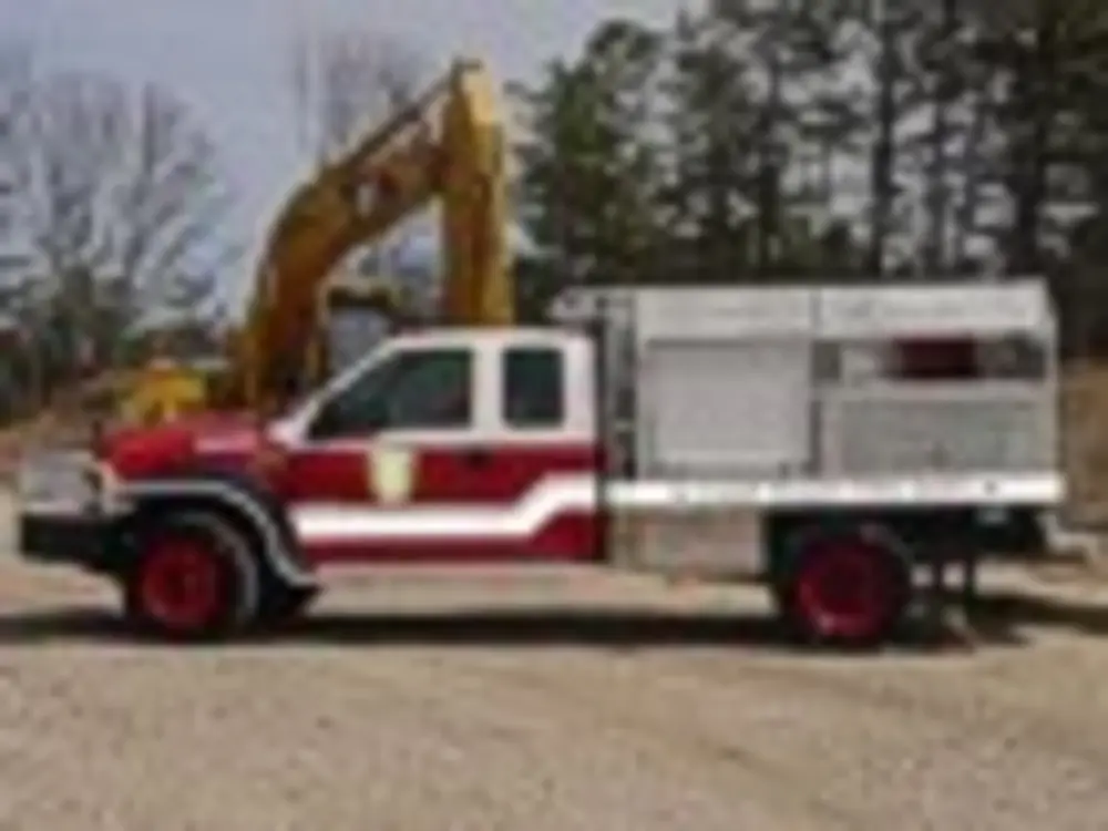 Exterior view of small fire truck showing cab, body compartments, and wheel/tire area.