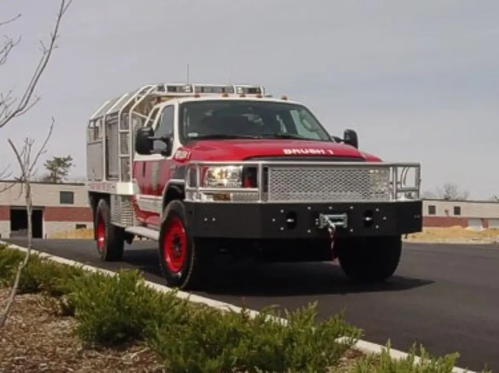 Exterior view of small fire truck showing cab, body compartments, and wheel/tire area.