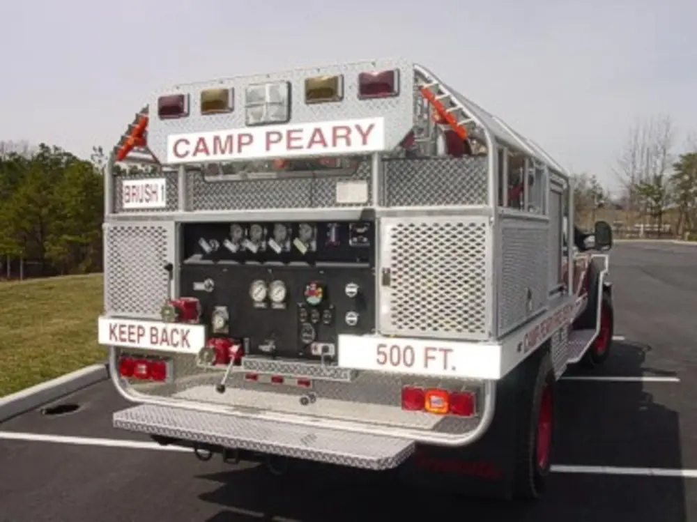 Exterior view of small fire truck showing cab, body compartments, and wheel/tire area.
