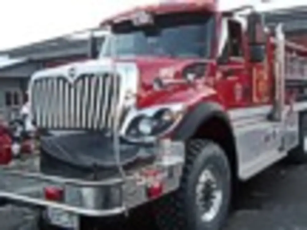 Exterior view of small fire truck showing cab, body compartments, and wheel/tire area.
