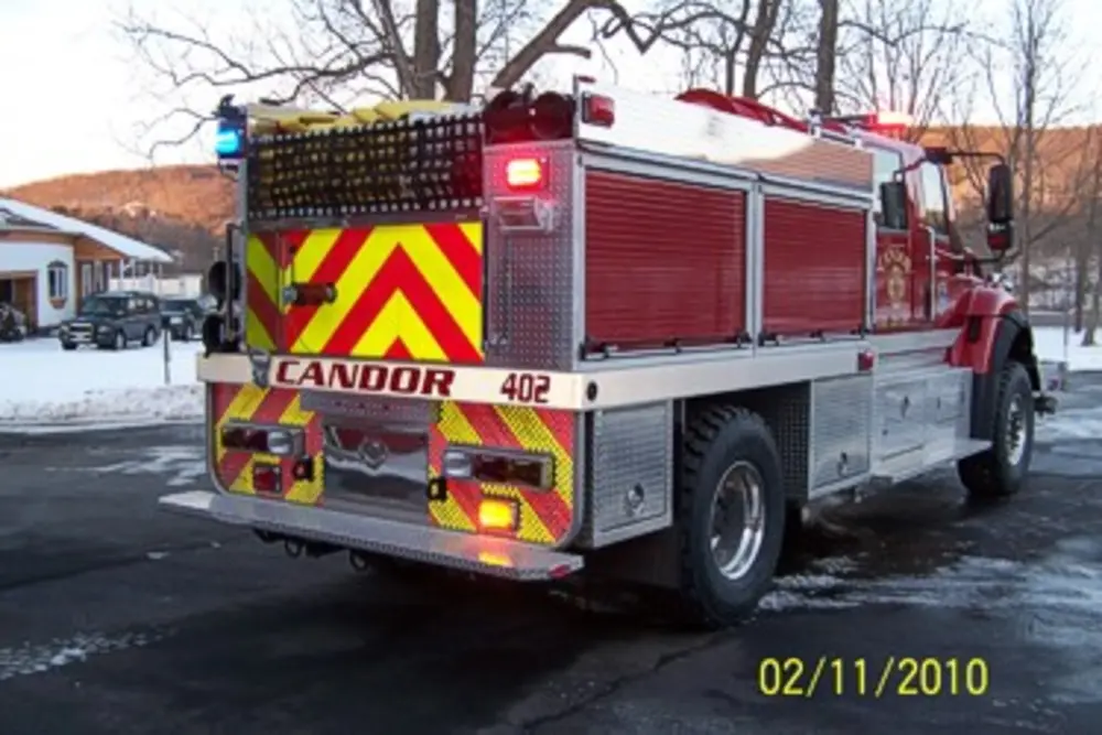 Exterior view of small fire truck showing cab, body compartments, and wheel/tire area.