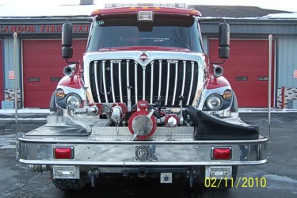 Exterior view of small fire truck showing cab, body compartments, and wheel/tire area.
