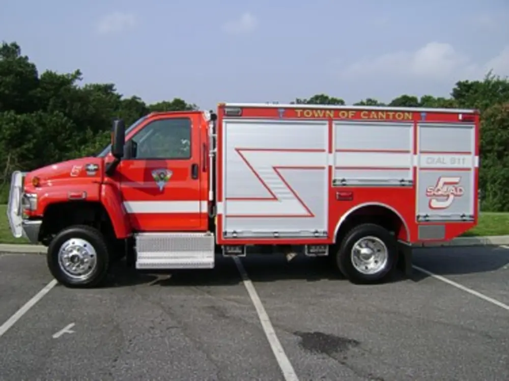Exterior view of small fire truck showing cab, body compartments, and wheel/tire area.