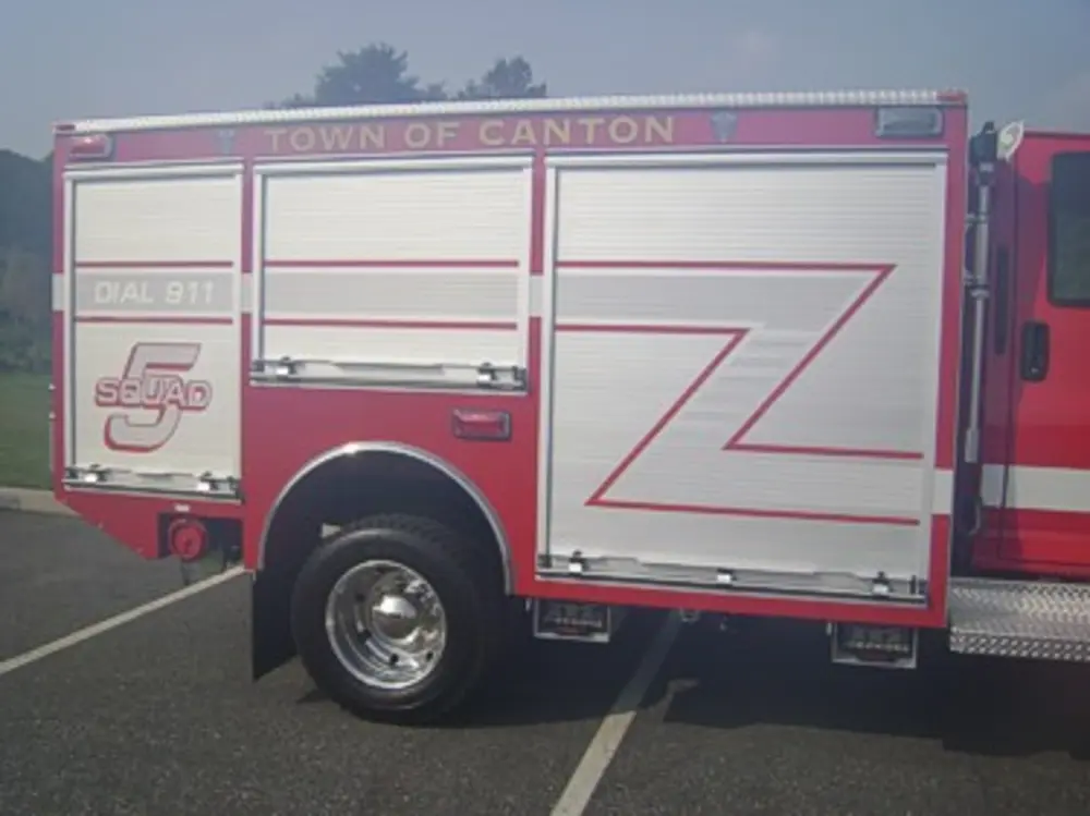 Exterior view of small fire truck showing cab, body compartments, and wheel/tire area.