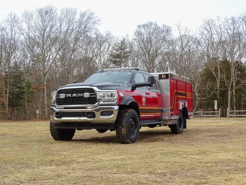 Exterior view of small fire truck showing cab, body compartments, and wheel/tire area.