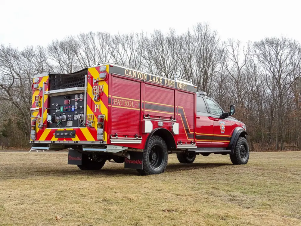 Exterior view of small fire truck showing cab, body compartments, and wheel/tire area.