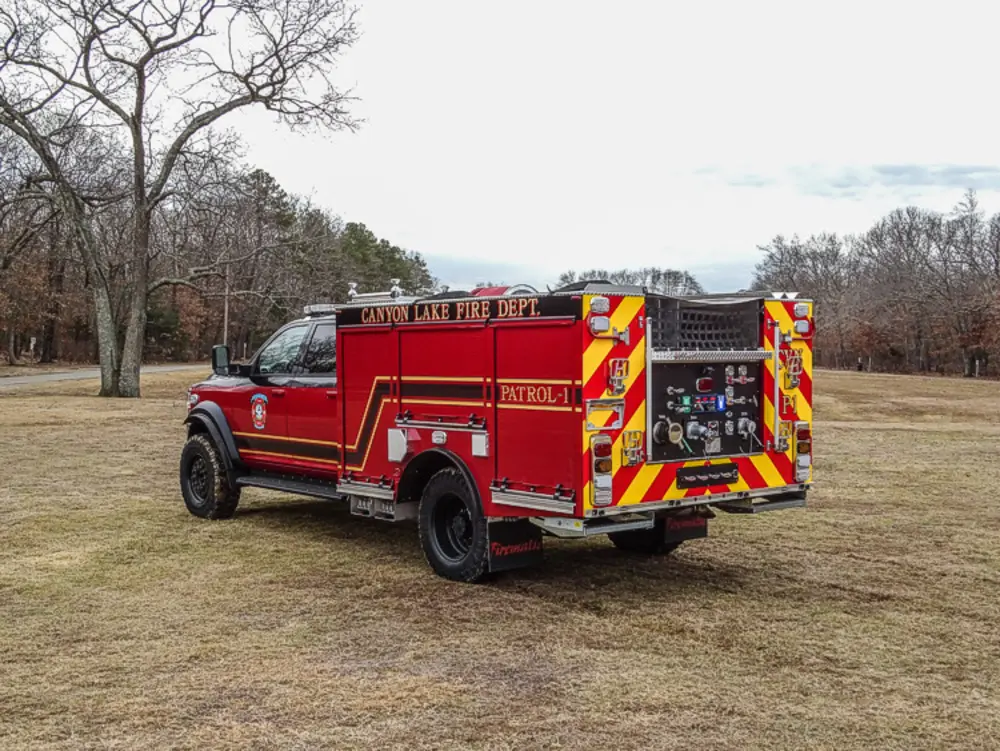 Exterior view of small fire truck showing cab, body compartments, and wheel/tire area.