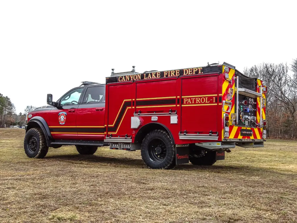 Exterior view of small fire truck showing cab, body compartments, and wheel/tire area.