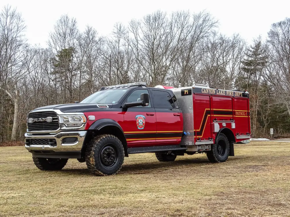 Exterior view of small fire truck showing cab, body compartments, and wheel/tire area.