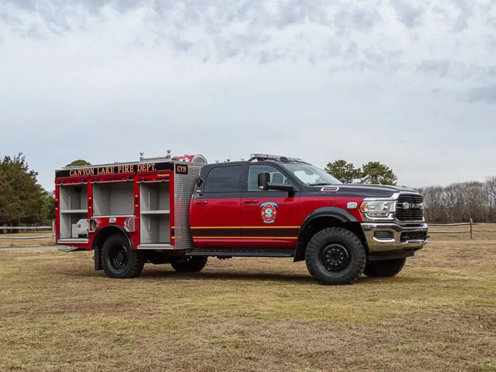 Exterior view of small fire truck showing cab, body compartments, and wheel/tire area.