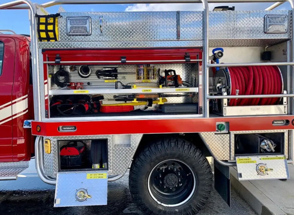 Exterior view of small fire truck showing cab, body compartments, and wheel/tire area.