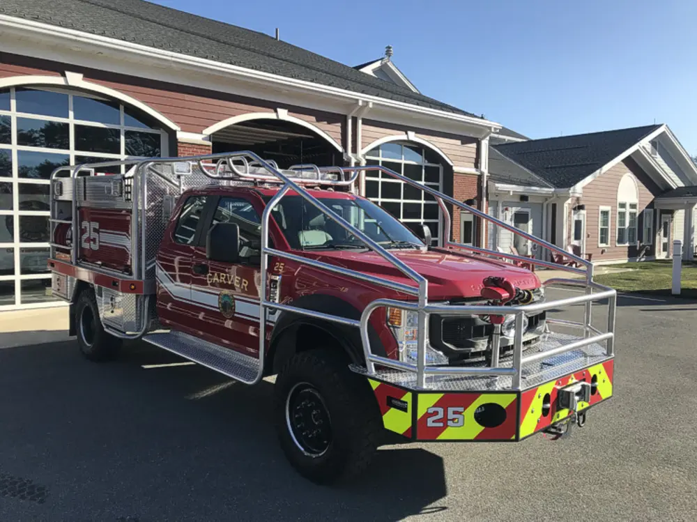 Exterior view of small fire truck showing cab, body compartments, and wheel/tire area.
