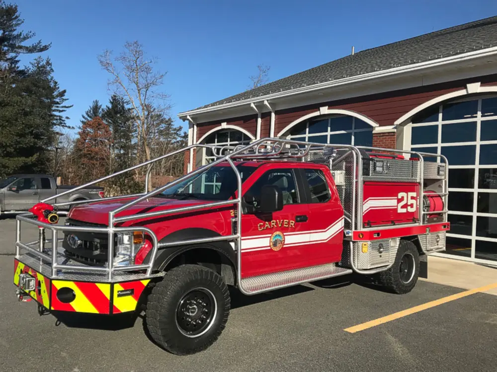 Exterior view of small fire truck showing cab, body compartments, and wheel/tire area.