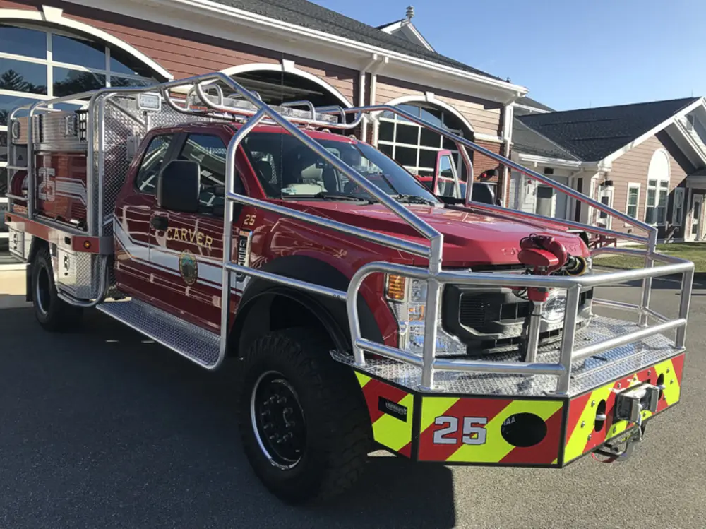 Exterior view of small fire truck showing cab, body compartments, and wheel/tire area.
