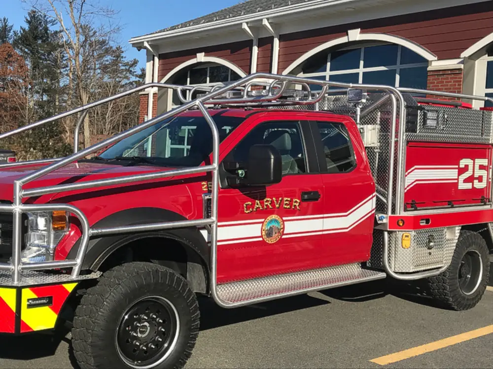 Exterior view of small fire truck showing cab, body compartments, and wheel/tire area.