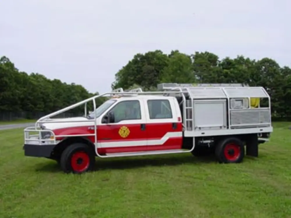 Exterior view of small fire truck showing cab, body compartments, and wheel/tire area.