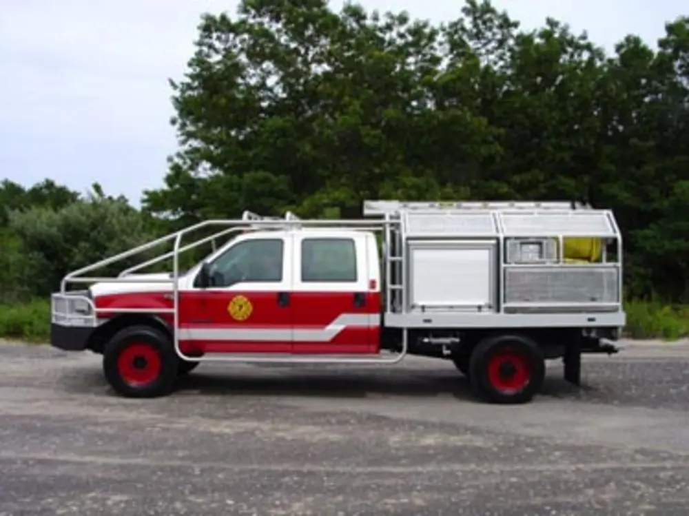 Exterior view of small fire truck showing cab, body compartments, and wheel/tire area.