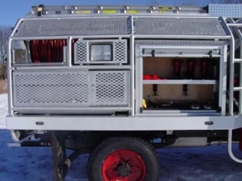 Exterior view of small fire truck showing cab, body compartments, and wheel/tire area.