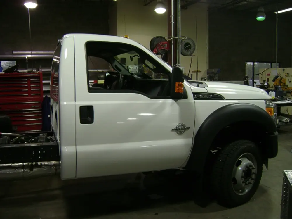 Exterior view of small fire truck showing cab, body compartments, and wheel/tire area.