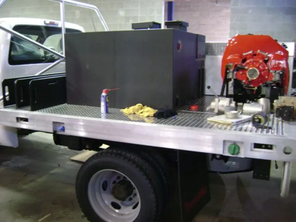 Exterior view of small fire truck showing cab, body compartments, and wheel/tire area.