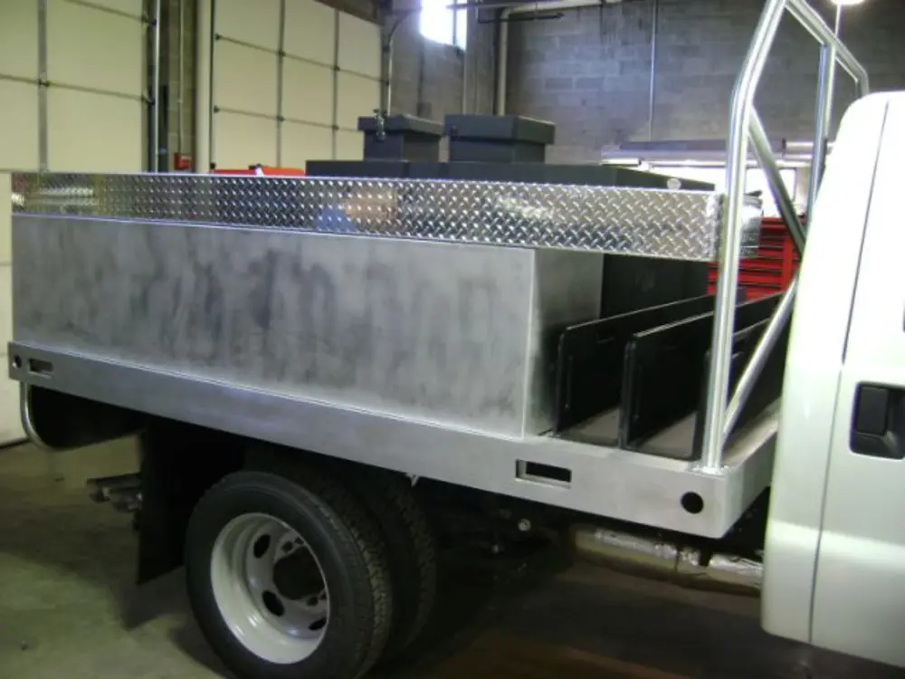 Exterior view of small fire truck showing cab, body compartments, and wheel/tire area.