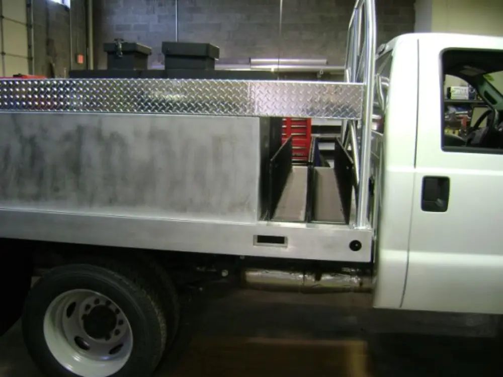 Exterior view of small fire truck showing cab, body compartments, and wheel/tire area.