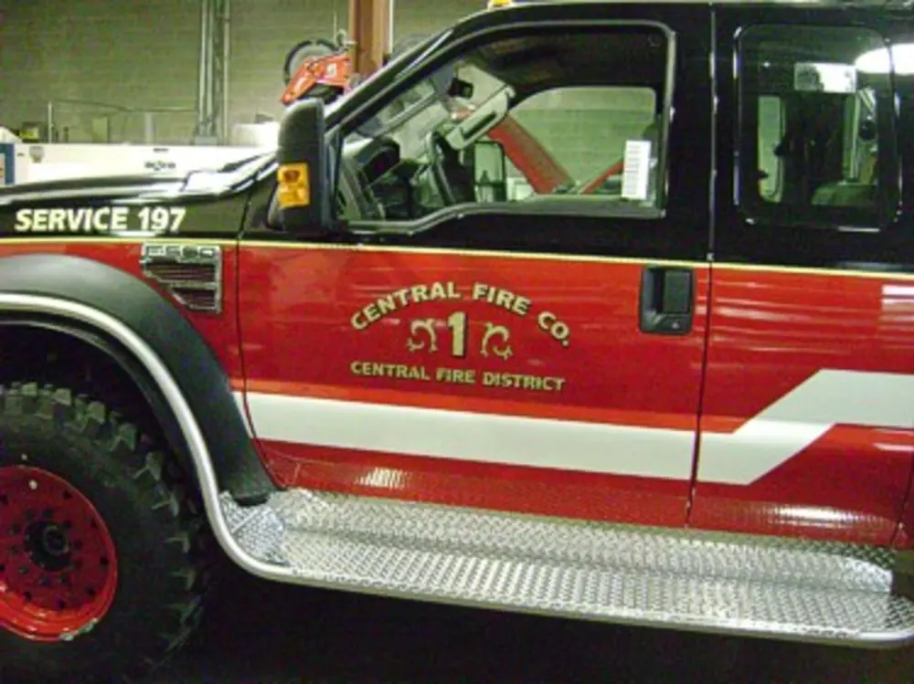 Exterior view of small fire truck showing cab, body compartments, and wheel/tire area.