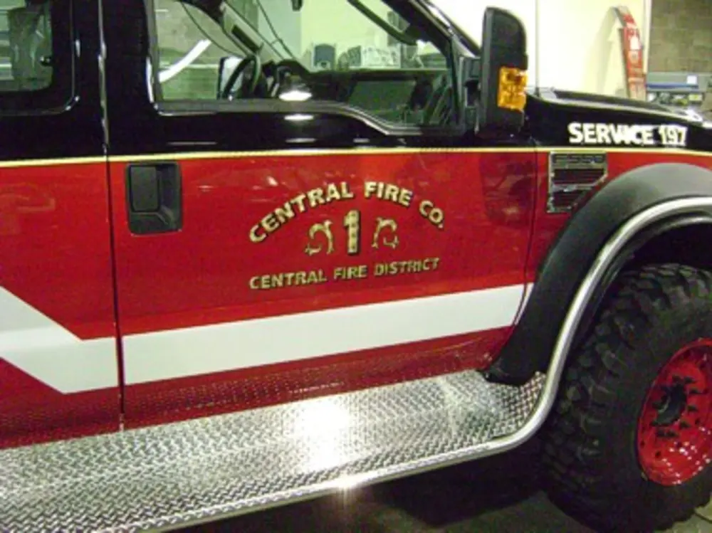 Exterior view of small fire truck showing cab, body compartments, and wheel/tire area.