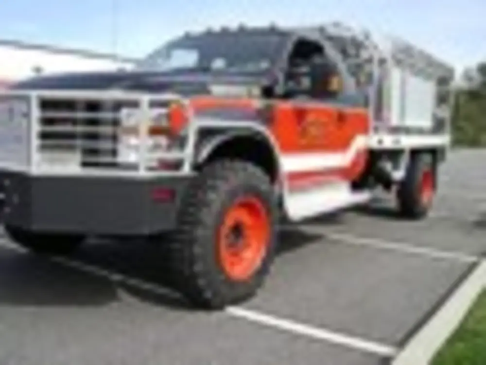 Exterior view of small fire truck showing cab, body compartments, and wheel/tire area.