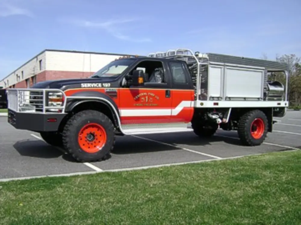 Exterior view of small fire truck showing cab, body compartments, and wheel/tire area.