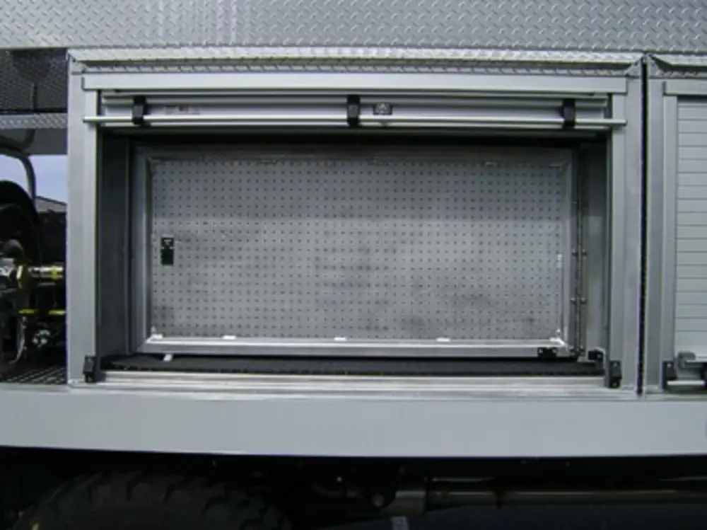 Exterior view of small fire truck showing cab, body compartments, and wheel/tire area.