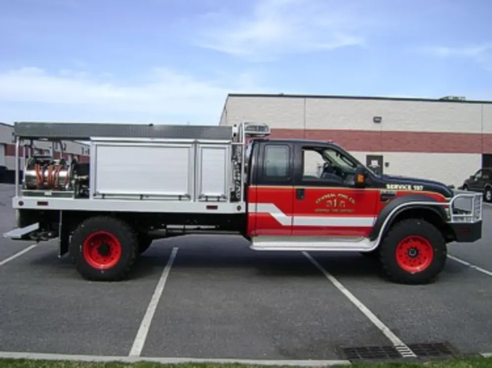 Exterior view of small fire truck showing cab, body compartments, and wheel/tire area.