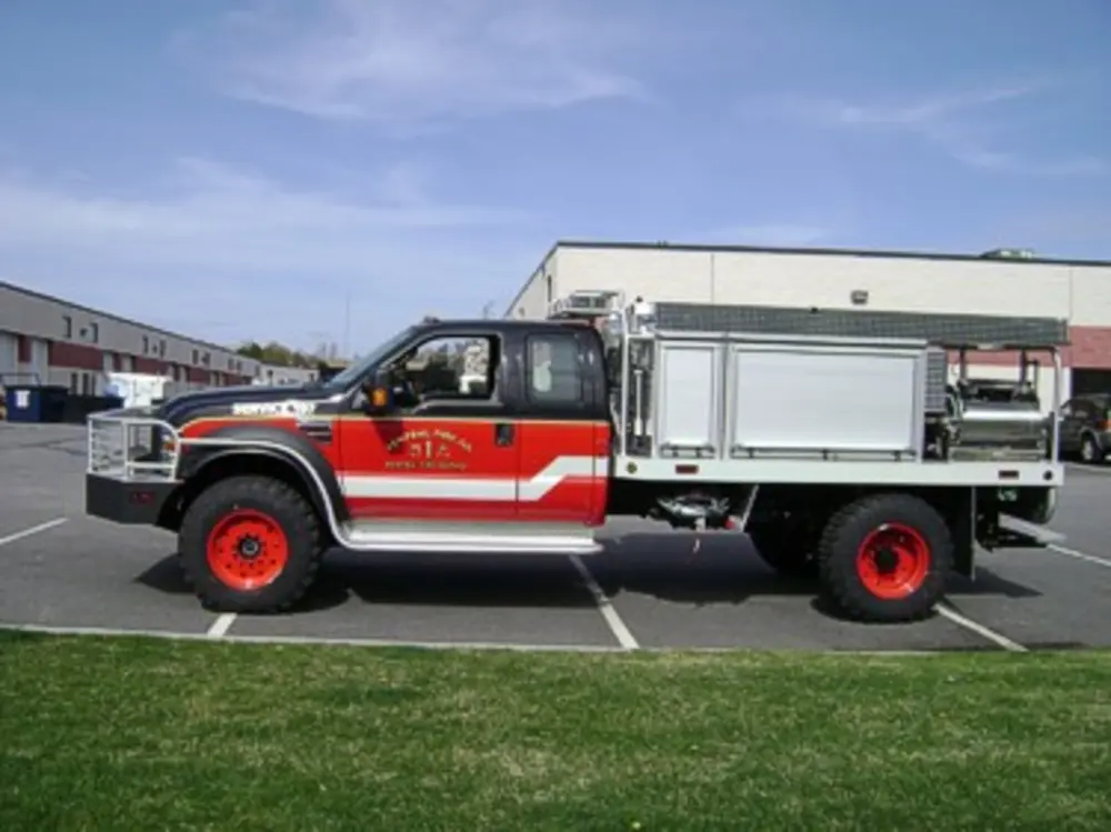 Exterior view of small fire truck showing cab, body compartments, and wheel/tire area.