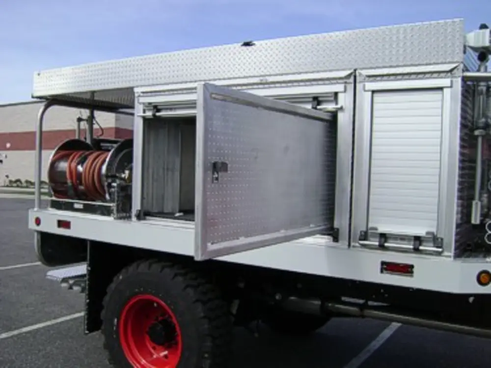 Exterior view of small fire truck showing cab, body compartments, and wheel/tire area.