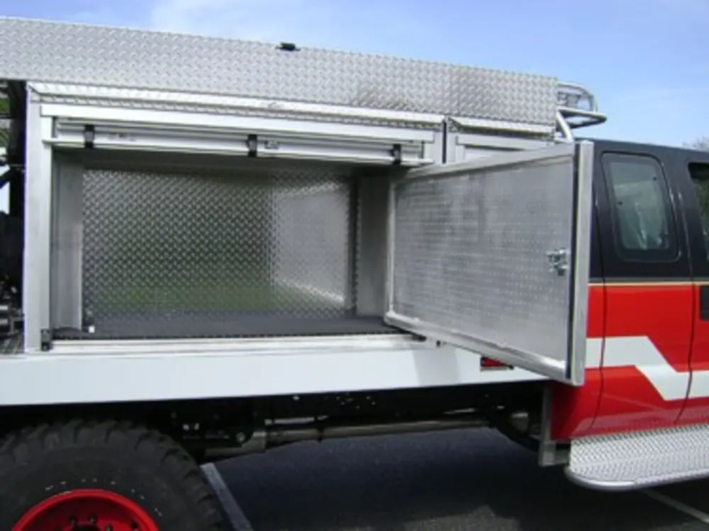 Exterior view of small fire truck showing cab, body compartments, and wheel/tire area.