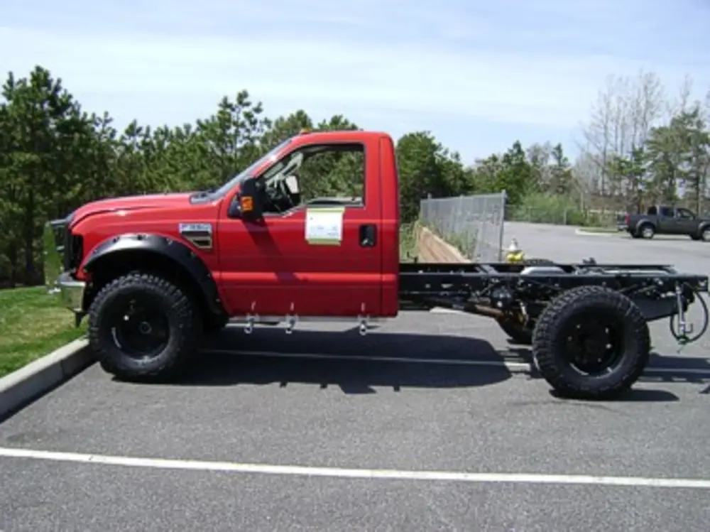 Exterior view of small fire truck showing cab, body compartments, and wheel/tire area.
