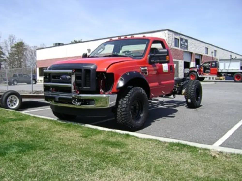 Exterior view of small fire truck showing cab, body compartments, and wheel/tire area.