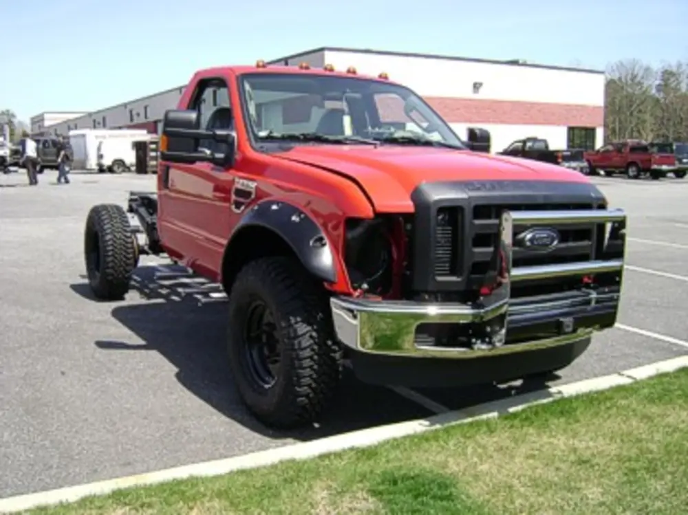 Exterior view of small fire truck showing cab, body compartments, and wheel/tire area.