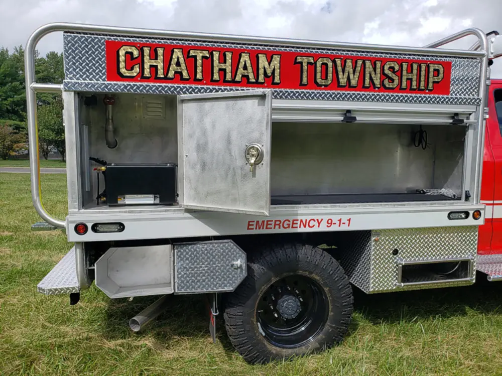Exterior view of small fire truck showing cab, body compartments, and wheel/tire area.