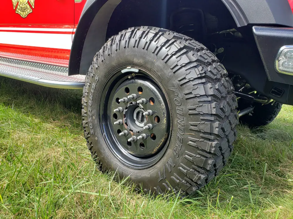 Exterior view of small fire truck showing cab, body compartments, and wheel/tire area.