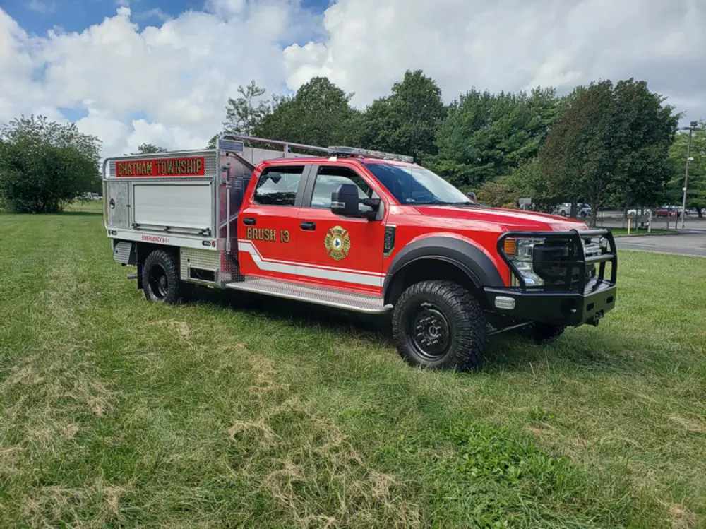 Exterior view of small fire truck showing cab, body compartments, and wheel/tire area.