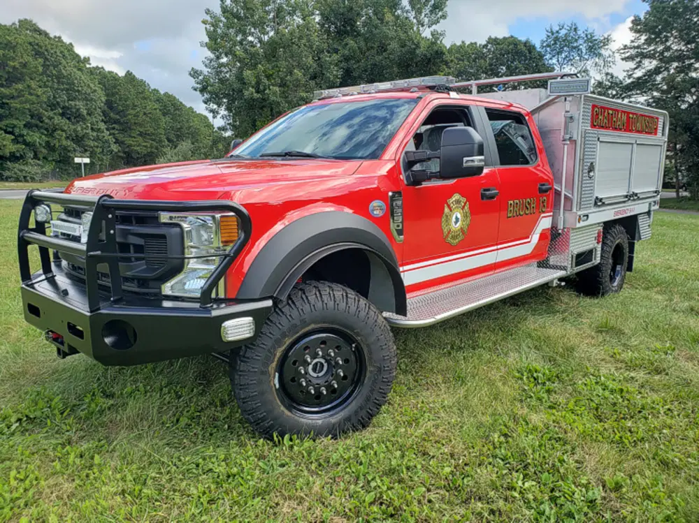 Exterior view of small fire truck showing cab, body compartments, and wheel/tire area.