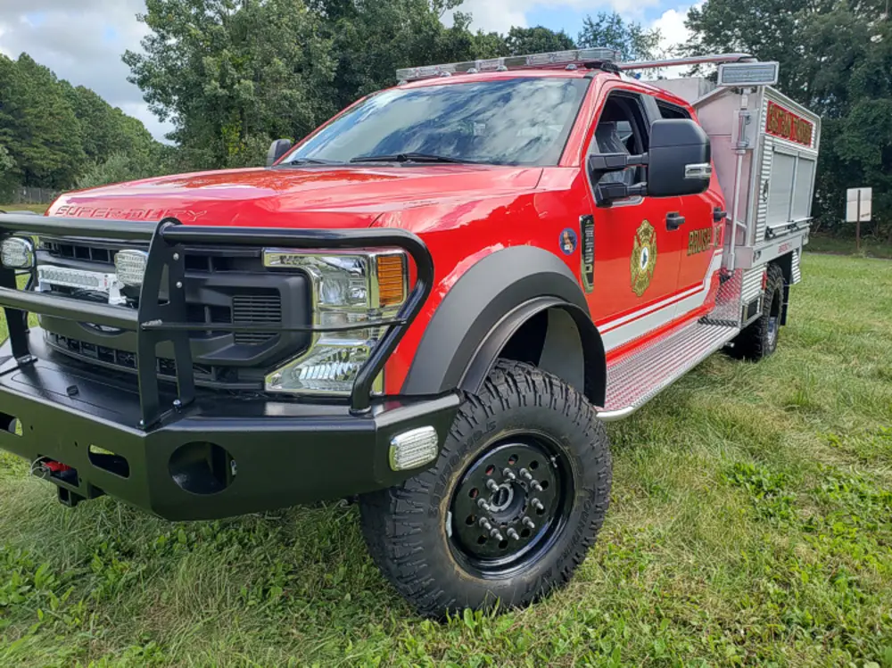 Exterior view of small fire truck showing cab, body compartments, and wheel/tire area.