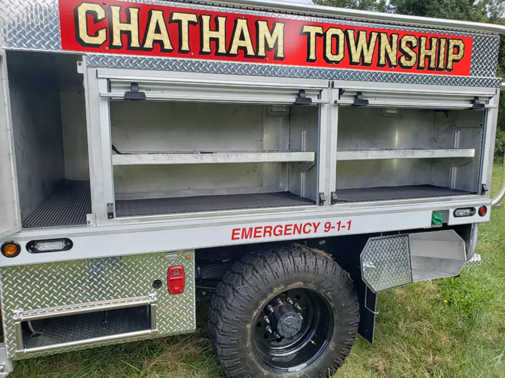 Exterior view of small fire truck showing cab, body compartments, and wheel/tire area.