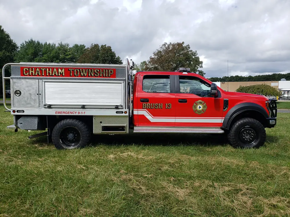 Exterior view of small fire truck showing cab, body compartments, and wheel/tire area.